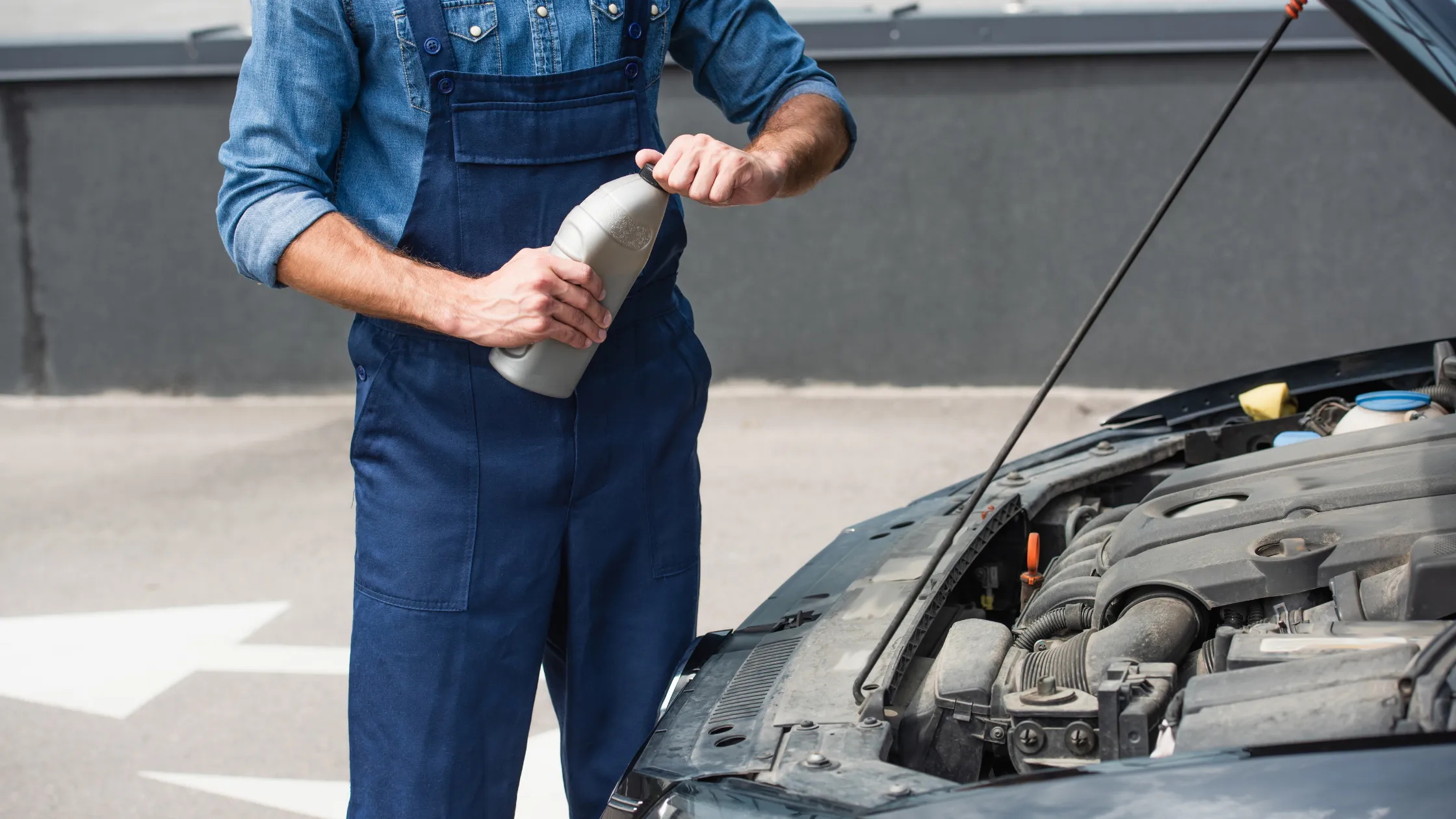 Mecánico-sosteniendo-una-botella-de-aceite-de-motor-cerca-del-automóvil-con-el-capo-abierto